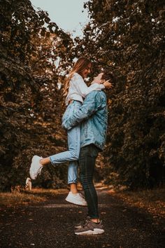 a man carrying a woman on his back while walking down a road in the woods