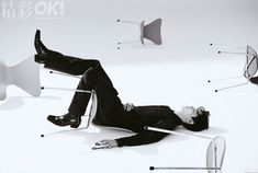 a man laying on top of a white chair next to two chairs with legs in the air