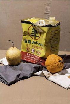 two oranges and an apple sitting on top of a table next to a bag