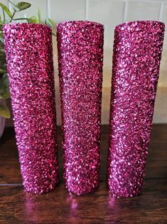 three pink glitter vases sitting on top of a wooden table next to a potted plant