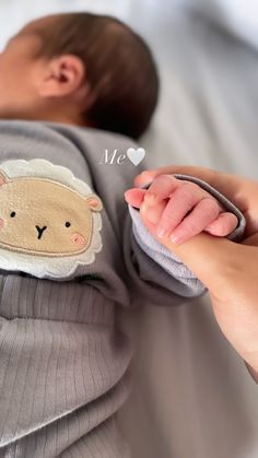 a baby laying on top of a bed next to a woman's hand with a small sheep applique on it