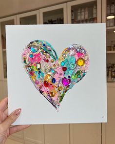 a hand holding up a card with a heart made out of buttons and sequins