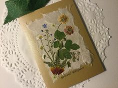 a card with flowers and leaves is on a doily next to a green leaf