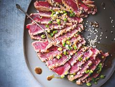 a plate topped with sliced up meat and garnished with sesame seeds on top