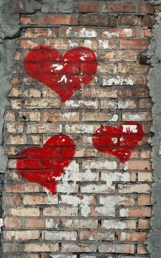 two hearts painted on a brick wall with paint peeling off the side and one red