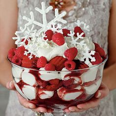 a woman holding a bowl filled with strawberries and whipped cream covered in snowflakes