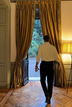 a man walking into a room with gold curtains on either side of the door and an open window