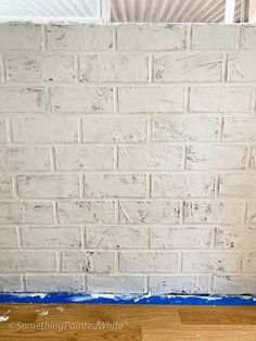 a white brick wall with blue tape on the floor and a window in the background