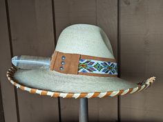 The Jasmine hat starts with a Gus fine palm hat body that is made in Mexico. It has a 4" brim and 5 1/2" crown. Hand laced in saddle color leather lace. The hatband has a layer of saddle tan suede that serves as the background for the beaded strip. The back of the band has 3 mini Conchos. Finished with a "red tail hawk" feather that is created from a turkey feather. Note: Hats are made to order. Allow up to 4 weeks for your hat to ship. Brimmed Toquilla Straw Hat For Western-themed Events, Handmade Fedora Hat Band From Toquilla Straw, Custom Curved Brim Straw Hat For Rodeo, Artisan Hat With Short Brim For Ranch, Flat Crown Felt Hat For Country Events In Summer, Summer Felt Hat With Flat Crown For Country Events, Artisan Short Brim Hat For Ranch, Artisan Style Brimmed Hats For Ranch, Artisan Fitted Hats For Ranch