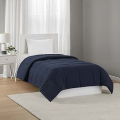 a bed in a room with white curtains and a blue comforter on top of it