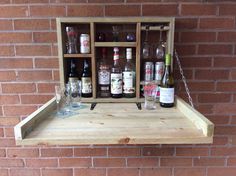 a wooden shelf with bottles and glasses hanging from it's sides on a brick wall