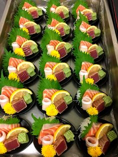 sushi platters are arranged on black plates with green leaves and yellow flowers around them