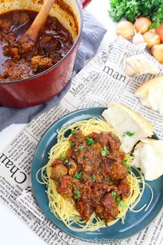 a blue plate topped with spaghetti and meat next to a pot of soup on top of a newspaper