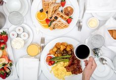 a person holding a coffee cup in front of a table full of breakfast foods and drinks