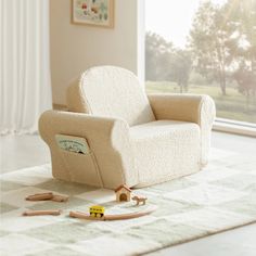 a white chair sitting on top of a rug next to a window with curtains and toys