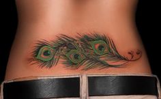 a woman's stomach with a peacock feather tattoo on her belly and the bottom part of her lower back