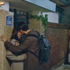 a man and woman standing next to each other near a wall with a backpack on it