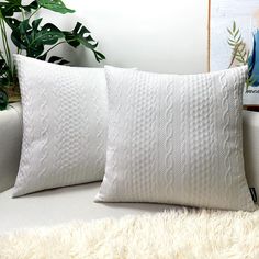 two white pillows sitting on top of a couch next to a potted green plant