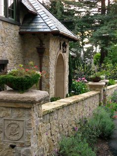 a stone house with potted plants on the front wall and side walk leading up to it