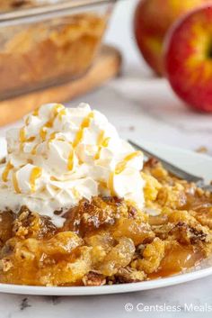 an apple crisp on a plate with whipped cream and two apples in the back ground