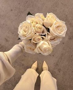 a bouquet of white roses is held by someone's feet on the cement floor