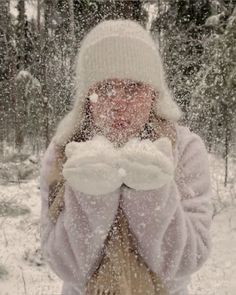 a woman standing in the snow with her hands covering her face and wearing a white hat