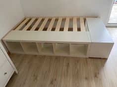 a white bed with wooden slats in a room next to a dresser and window