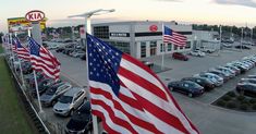 several american flags are lined up in front of a car dealership with cars parked on the lot