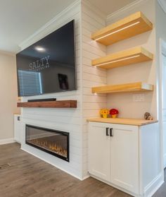 a tv mounted on the wall above a fireplace in a room with white walls and wood flooring