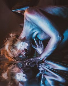 a naked woman laying on top of a table next to a glass floor covered in liquid