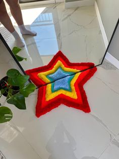 a red, yellow and blue star shaped rug on the floor next to a potted plant