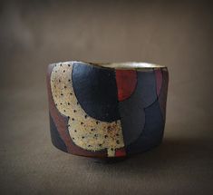 a close up of a bracelet on a brown surface with black, red and yellow designs