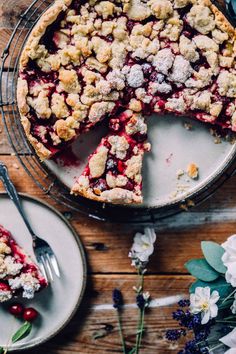 a pie with cranberry toppings on a wooden table next to plates and flowers