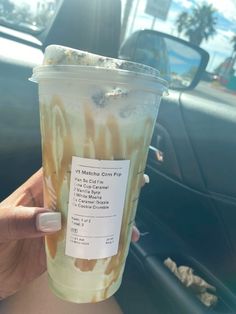 a person holding up a cup with ice cream on it in front of a car