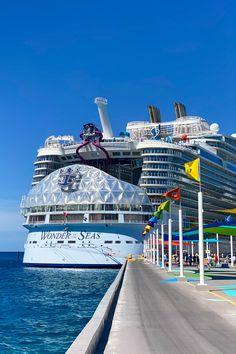 a cruise ship docked in the ocean next to a pier with flags and umbrellas