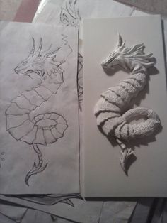 some paper with drawings on them and one has a dragon in the middle next to it