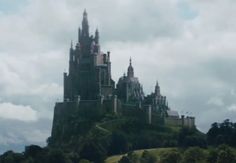 a castle on top of a hill in the middle of some trees and clouds above it