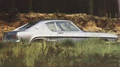 an old car sitting in the middle of some tall grass and dirt with trees in the background