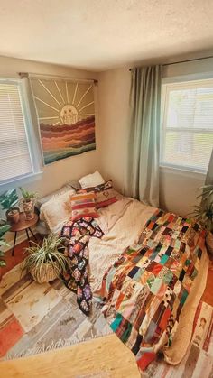 a bed sitting in a bedroom next to two windows with plants on top of it