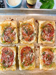 small square pizzas with cheese and tomato sauce on a baking sheet next to a bottle of wine