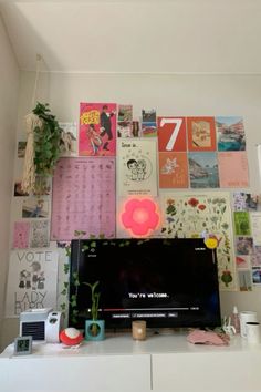 a flat screen tv sitting on top of a white dresser next to a wall covered in posters