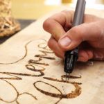 a person writing on a piece of wood with a pen