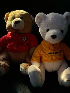 two teddy bears sitting next to each other on a black surface with one wearing a yellow shirt