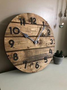 a large wooden clock sitting on top of a table next to a potted plant