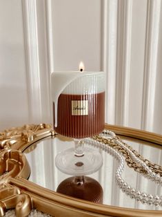 a candle sitting on top of a glass table next to a gold plate and chain