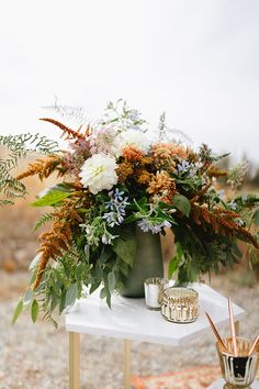 an arrangement of flowers and greenery on a white table with a gold cup next to it