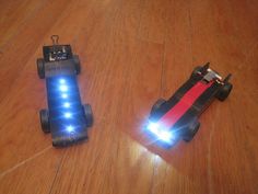 two toy cars sitting on top of a wooden floor next to each other with lights