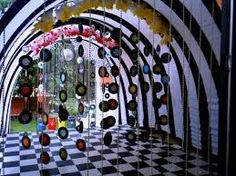 an art installation made out of glass bottles and chains on a checkered floor with flowers hanging from the ceiling