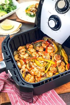 an air fryer filled with shrimp and peppers on top of a wooden cutting board