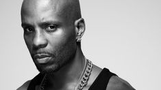 a bald man wearing a black tank top and silver chains on his neck is looking at the camera